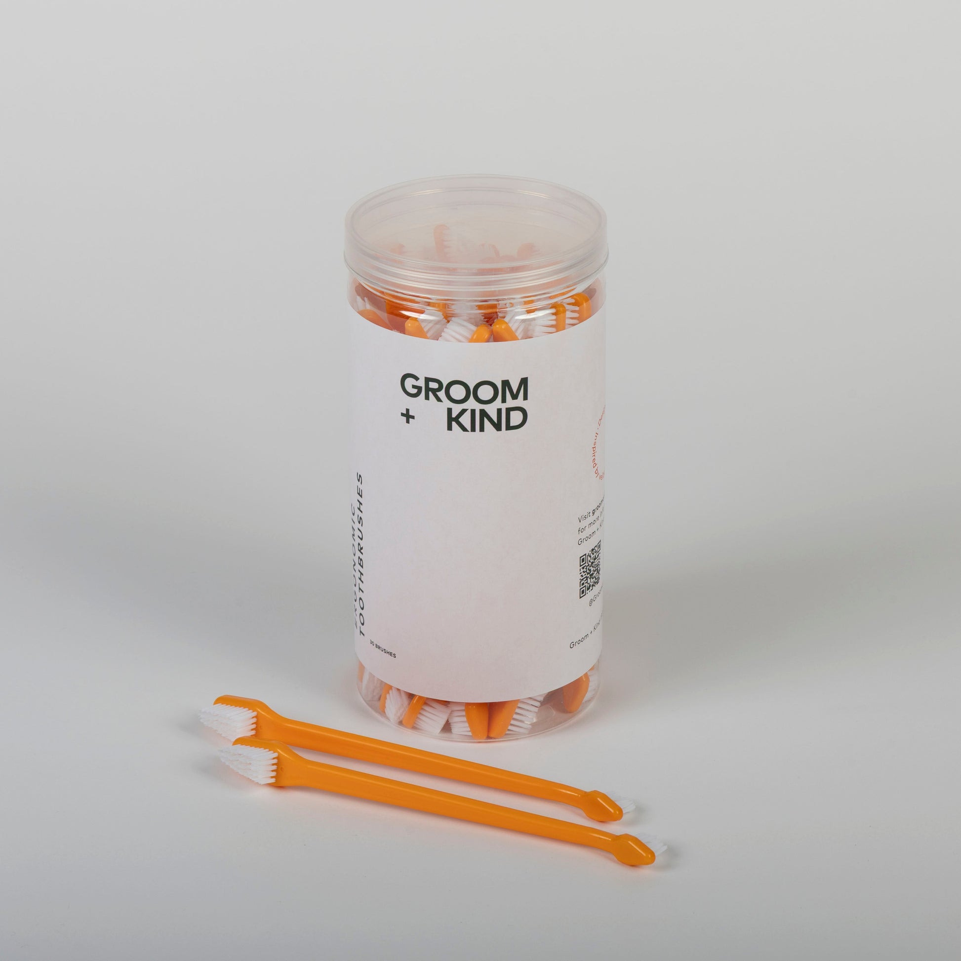 Jar of professional toothbrushes labeled 'Groom + Kind' on a white background