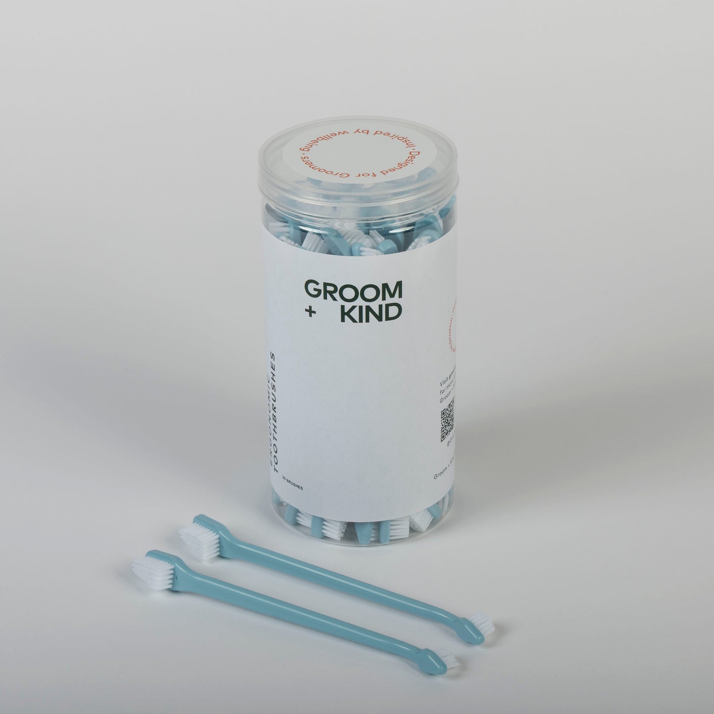 Jar of professional toothbrushes labeled 'Groom + Kind' on a white background
