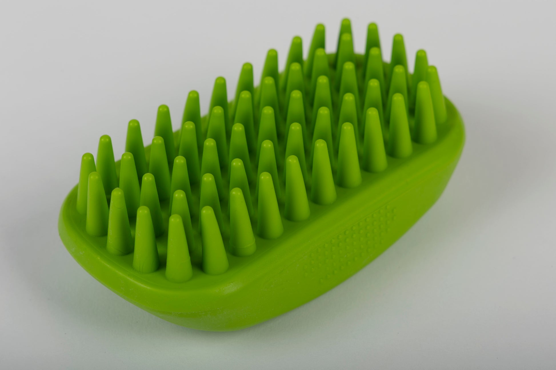 Green grooming brush with textured surface on a white background