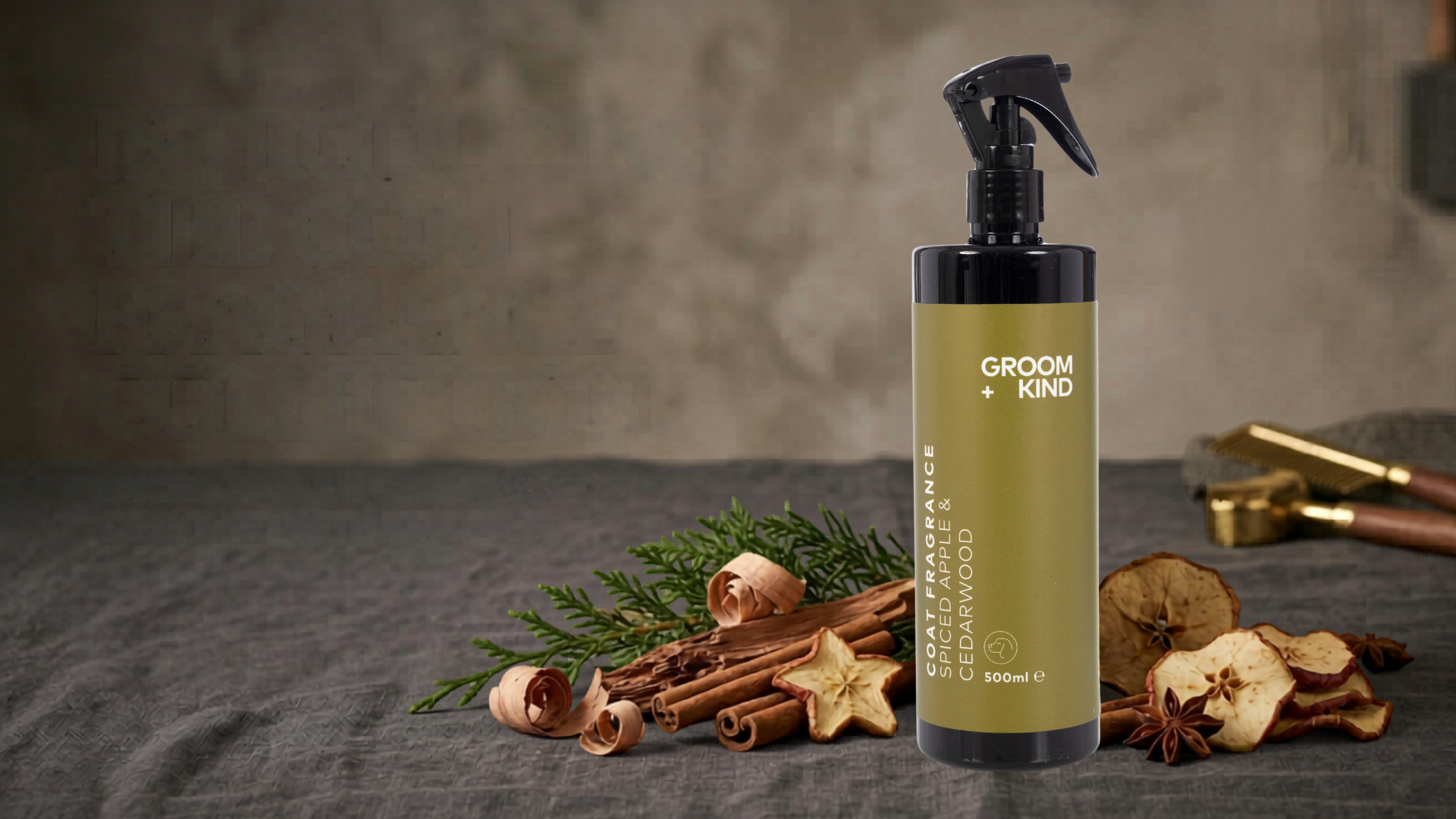 Bottle of Groom & Kind spiced apple and cedarwood coat fragrance with cinnamon sticks and spiced apple on a dark linen surface.
